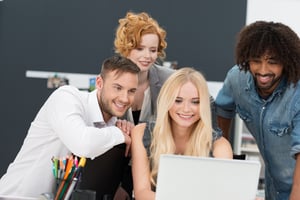 Happy multiethnic diverse group of young business people grouped around a laptop computer smiling as they look at data on the screen