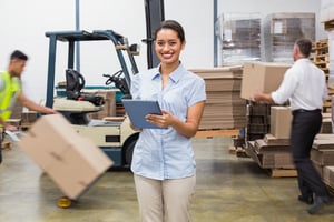 Smiling manager using digital tablet during busy period in a large warehouse