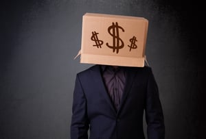 Young man standing and gesturing with a cardboard box on his head with dollar signs